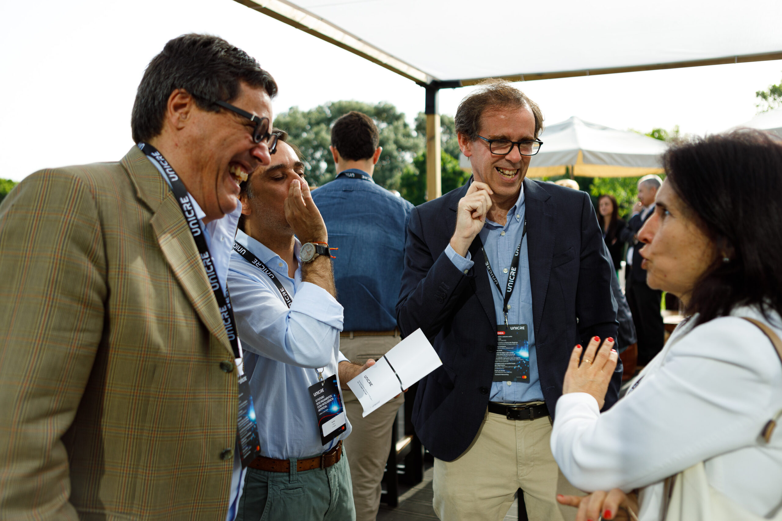 Group of professionals at an outdoor event, conversing and showing name badges and documents.