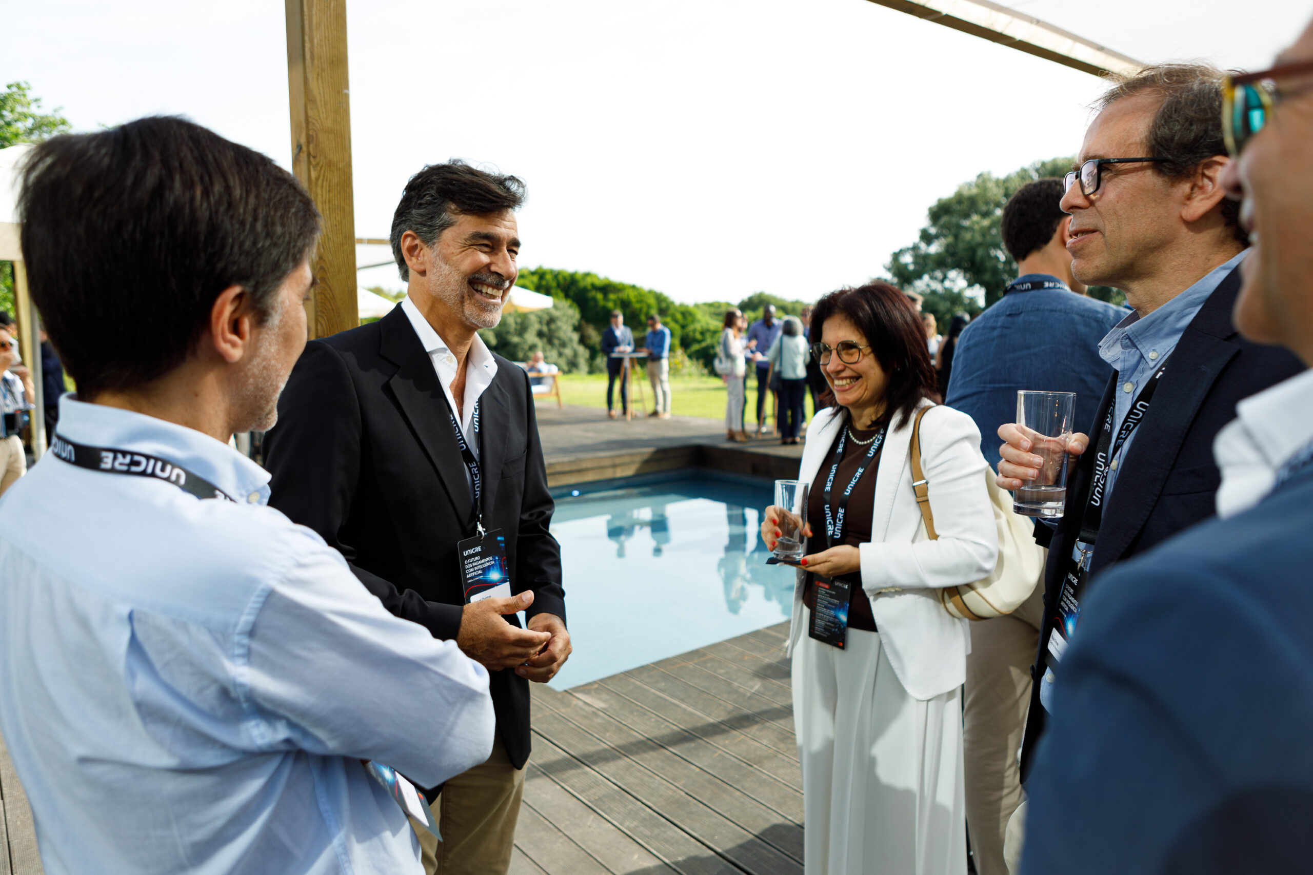 Professionals chatting and smiling at an outdoor networking event by a pool, wearing lanyard badges.