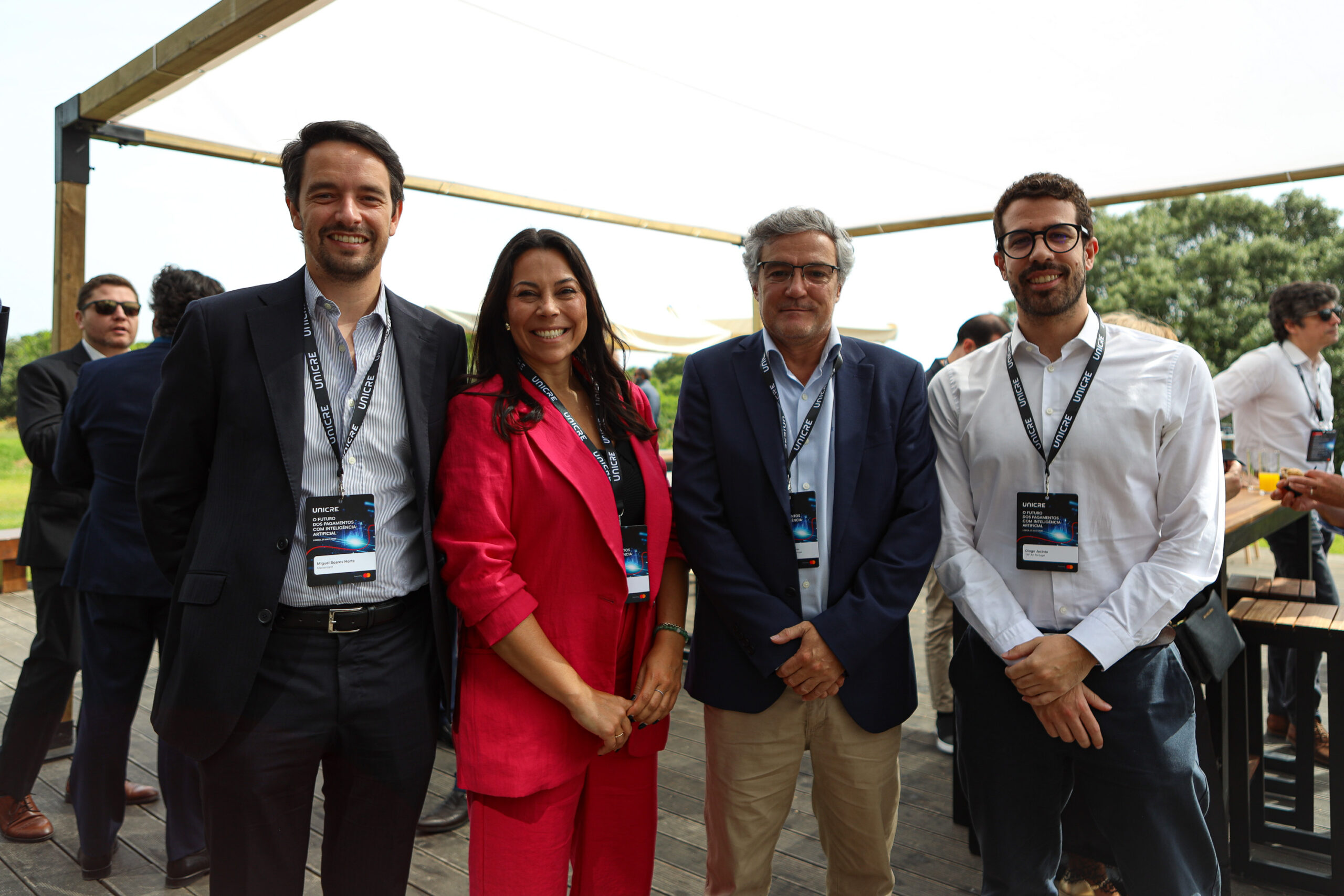 Group of four professionals posing outdoors at a conference, wearing lanyards and badges and smiling at the camera.